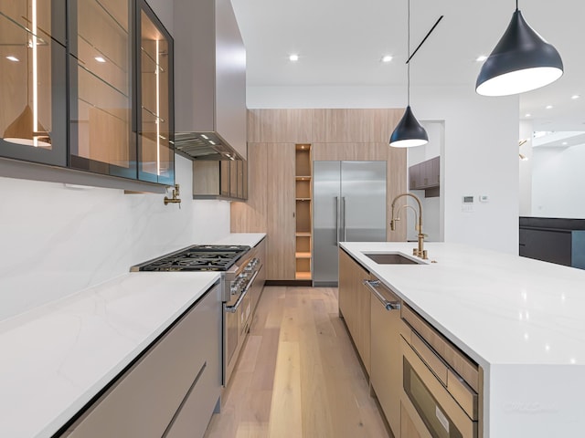 kitchen with light stone countertops, premium appliances, wall chimney range hood, light hardwood / wood-style floors, and hanging light fixtures