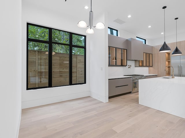 kitchen with sink, wall chimney range hood, light stone counters, pendant lighting, and high end appliances