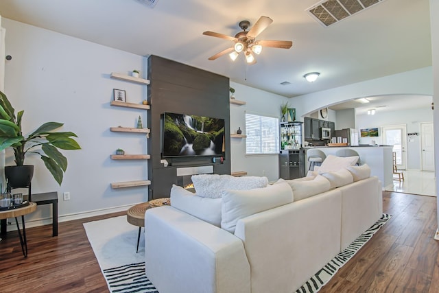 living room with dark hardwood / wood-style flooring, a large fireplace, and ceiling fan