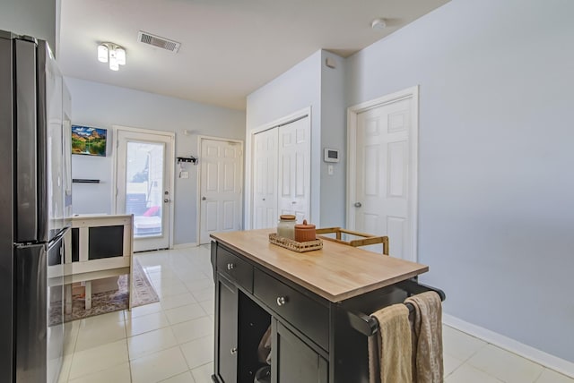 kitchen featuring butcher block countertops, a center island, light tile patterned floors, and stainless steel refrigerator