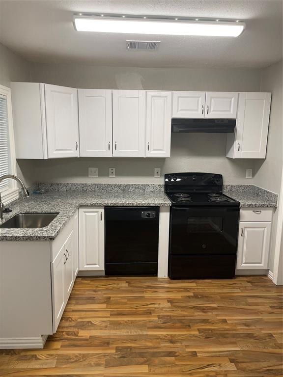 kitchen with light stone countertops, sink, white cabinets, black appliances, and hardwood / wood-style flooring