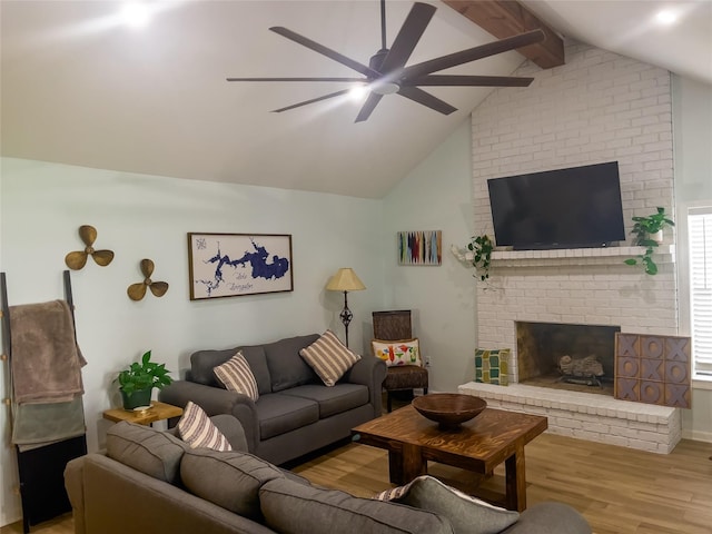 living room featuring vaulted ceiling with beams, ceiling fan, light hardwood / wood-style floors, and a brick fireplace