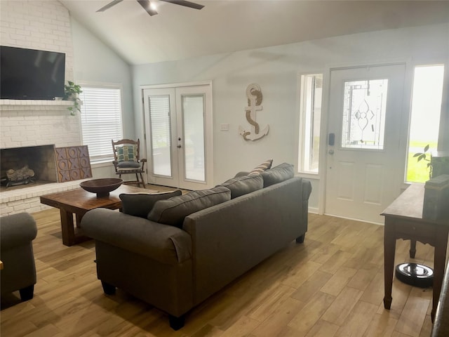 living room with ceiling fan, french doors, a brick fireplace, light hardwood / wood-style floors, and vaulted ceiling