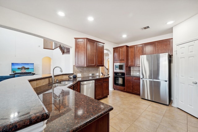 kitchen featuring sink, decorative backsplash, dark stone countertops, light tile patterned floors, and appliances with stainless steel finishes