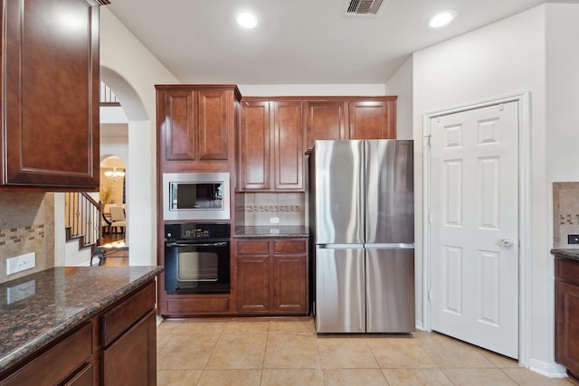 kitchen with dark stone countertops, light tile patterned floors, appliances with stainless steel finishes, and tasteful backsplash