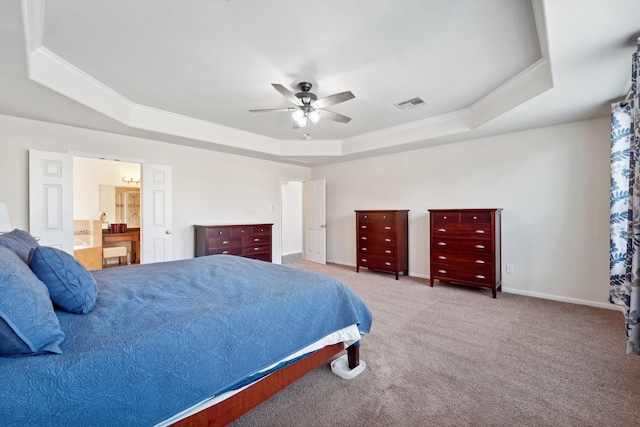 bedroom with light carpet, a tray ceiling, ceiling fan, crown molding, and connected bathroom