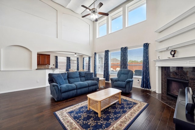 living room with a premium fireplace, ceiling fan, dark wood-type flooring, and a high ceiling