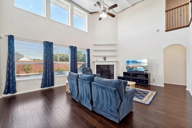 living room featuring ceiling fan, dark hardwood / wood-style flooring, a towering ceiling, and a tiled fireplace