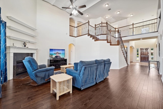 living room featuring a towering ceiling, dark hardwood / wood-style floors, ceiling fan, and a tiled fireplace