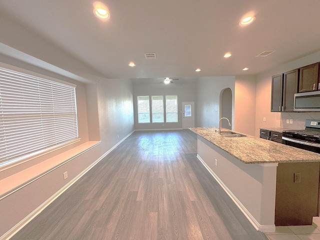 kitchen featuring light stone countertops, sink, ceiling fan, dark hardwood / wood-style floors, and a center island with sink