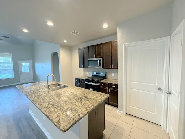 kitchen featuring gas stove, light stone countertops, sink, backsplash, and an island with sink