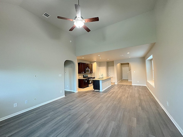 unfurnished living room with ceiling fan, dark hardwood / wood-style flooring, sink, and a high ceiling