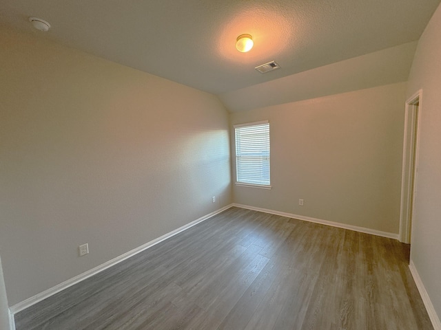 empty room featuring wood-type flooring, a textured ceiling, and vaulted ceiling