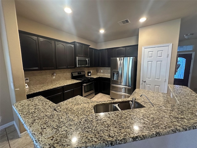 kitchen with sink, light stone countertops, light tile patterned floors, tasteful backsplash, and stainless steel appliances