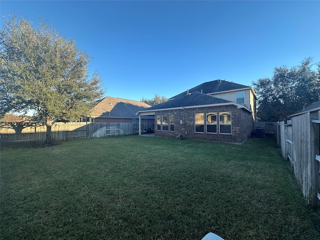 back of house featuring a lawn, a fenced backyard, and brick siding