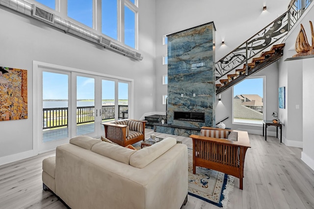 living room featuring a large fireplace, a water view, a high ceiling, and light wood-type flooring