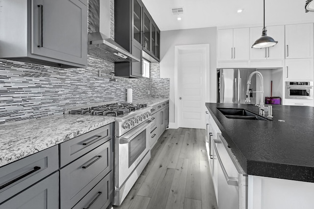 kitchen featuring pendant lighting, wall chimney range hood, sink, appliances with stainless steel finishes, and white cabinetry