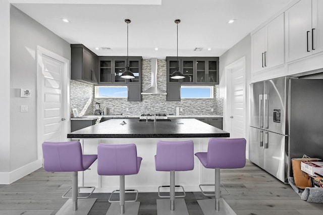 kitchen featuring stainless steel refrigerator with ice dispenser, a kitchen island, hanging light fixtures, and wall chimney exhaust hood