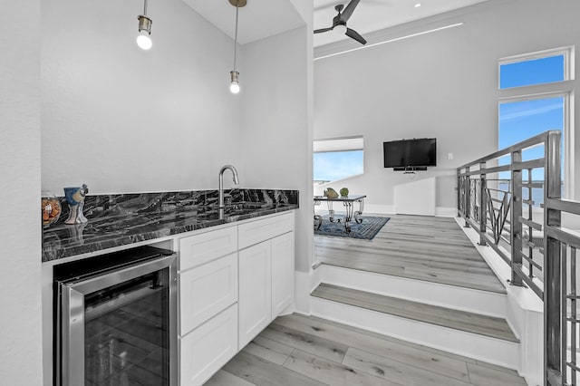 kitchen with ceiling fan, beverage cooler, sink, pendant lighting, and white cabinets