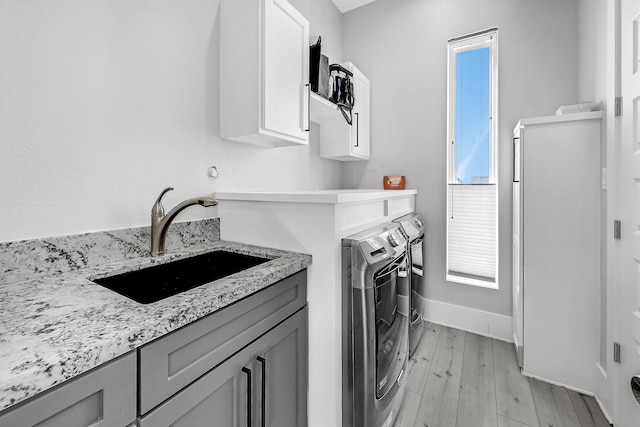 laundry room featuring washer and dryer, light hardwood / wood-style flooring, cabinets, and sink