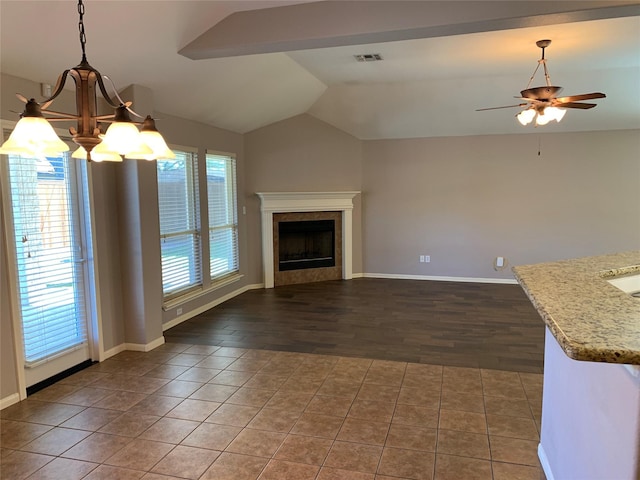 unfurnished living room with ceiling fan with notable chandelier, vaulted ceiling, and dark tile patterned flooring