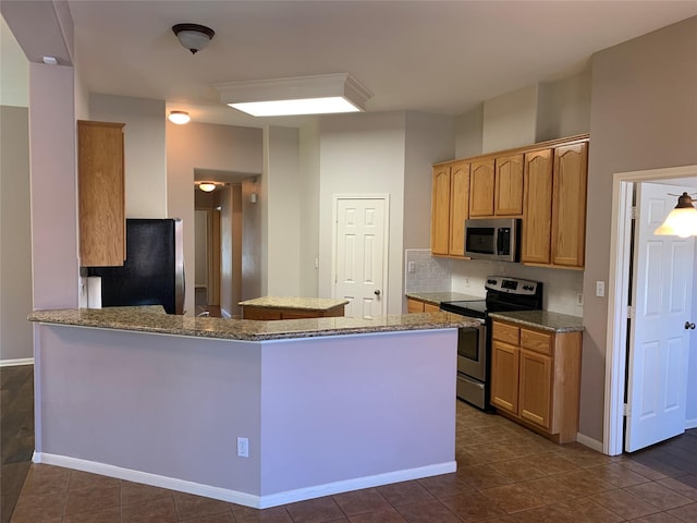 kitchen featuring kitchen peninsula, appliances with stainless steel finishes, tasteful backsplash, dark tile patterned flooring, and stone counters