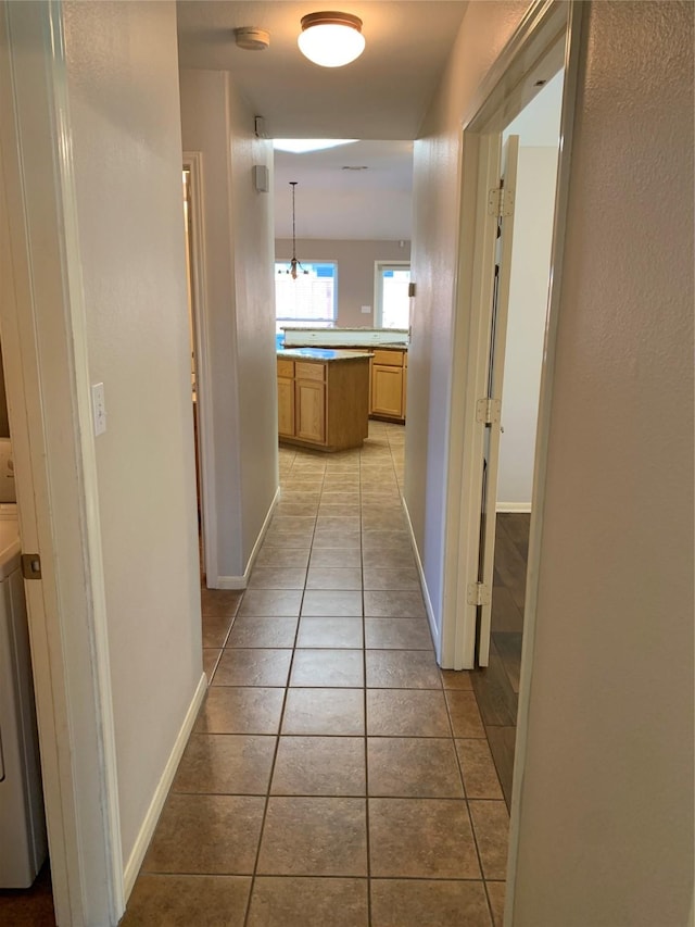 hallway featuring light tile patterned flooring, washer / dryer, and a chandelier