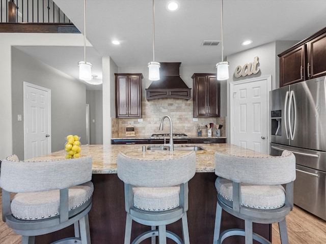 kitchen with backsplash, premium range hood, a spacious island, hanging light fixtures, and stainless steel fridge with ice dispenser