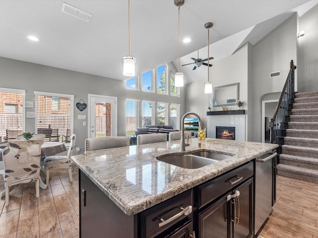 kitchen featuring dark brown cabinetry, light stone countertops, sink, pendant lighting, and a kitchen island with sink