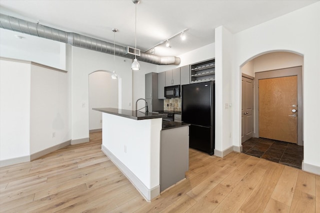 kitchen featuring light wood-type flooring, gray cabinetry, black appliances, a center island with sink, and hanging light fixtures