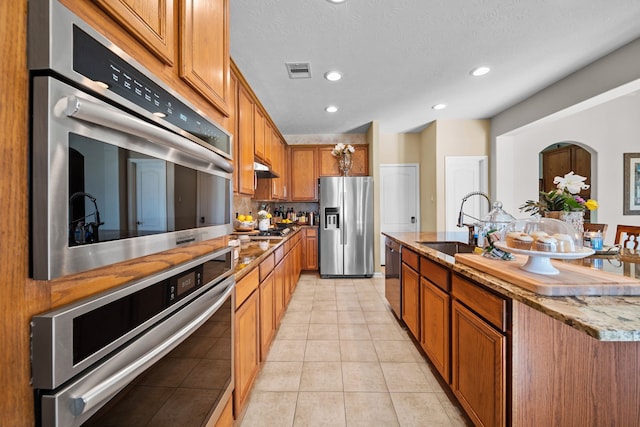 kitchen featuring a kitchen island with sink, sink, light tile patterned floors, tasteful backsplash, and stainless steel appliances