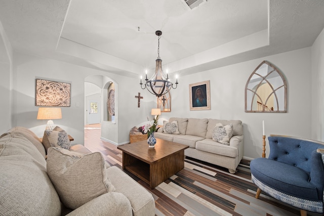 living room featuring a raised ceiling, light hardwood / wood-style flooring, and an inviting chandelier