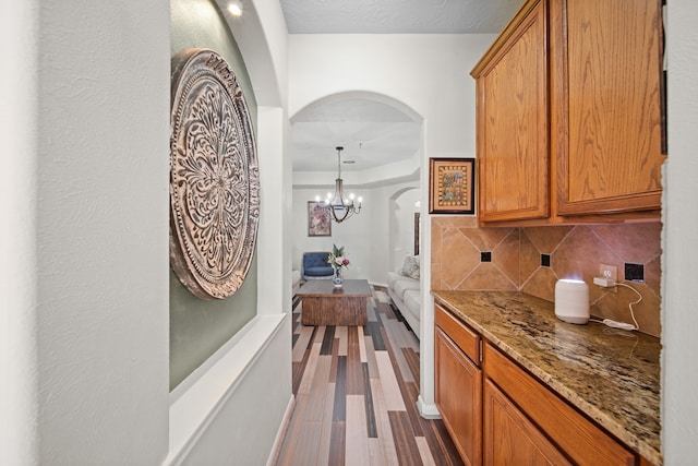 kitchen with light stone countertops, hanging light fixtures, a notable chandelier, backsplash, and wood-type flooring