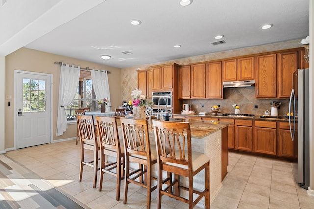 kitchen featuring a kitchen breakfast bar, light tile patterned floors, an island with sink, and appliances with stainless steel finishes