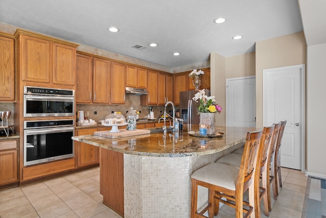 kitchen featuring stone counters, sink, a breakfast bar area, light tile patterned flooring, and appliances with stainless steel finishes