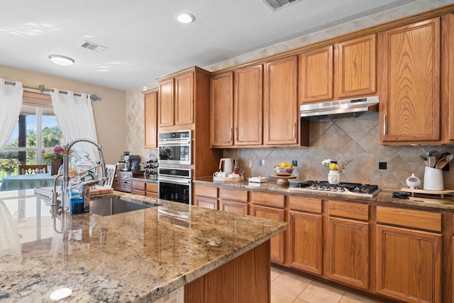 kitchen with light stone countertops, appliances with stainless steel finishes, tasteful backsplash, sink, and light tile patterned floors