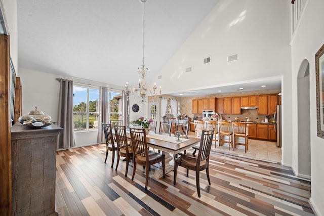 dining area with light hardwood / wood-style flooring, high vaulted ceiling, and a notable chandelier