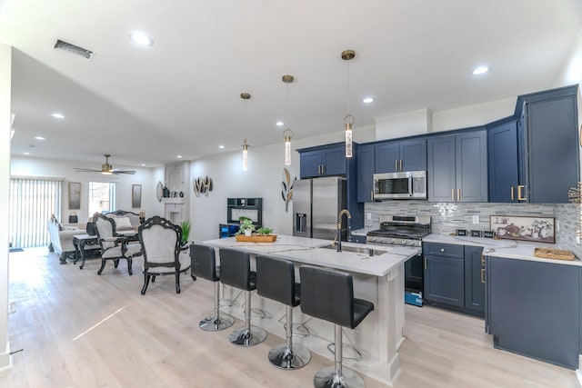 kitchen with light stone countertops, appliances with stainless steel finishes, ceiling fan, decorative light fixtures, and an island with sink