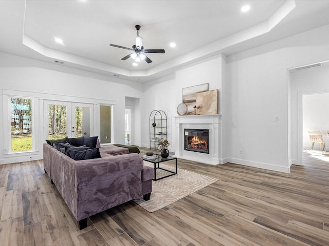 living room featuring ceiling fan, a raised ceiling, light wood-type flooring, and french doors