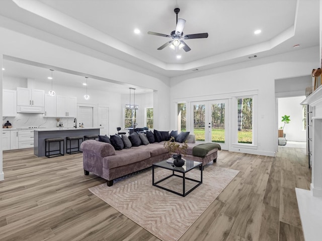 living room with french doors, light wood-type flooring, a raised ceiling, ceiling fan, and sink