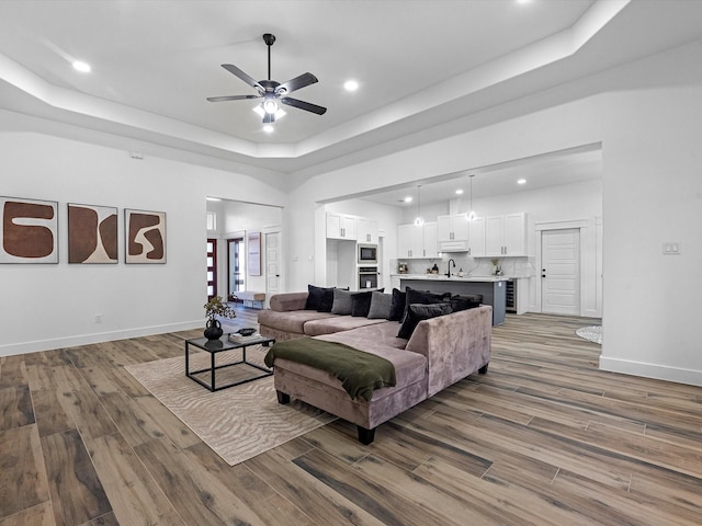 living room with ceiling fan, a raised ceiling, and wood-type flooring