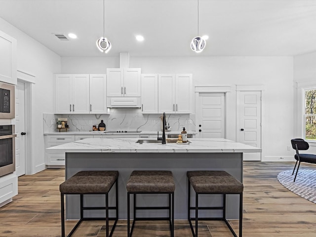 kitchen with a kitchen island with sink, white cabinets, and decorative light fixtures