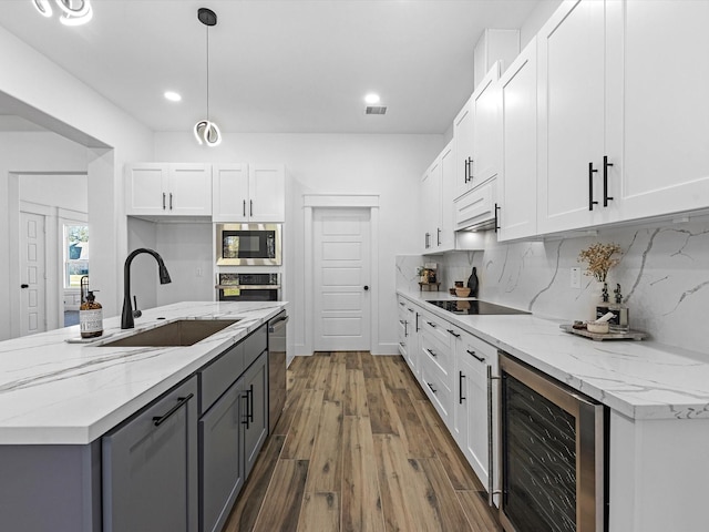 kitchen with stainless steel appliances, beverage cooler, sink, white cabinetry, and hanging light fixtures