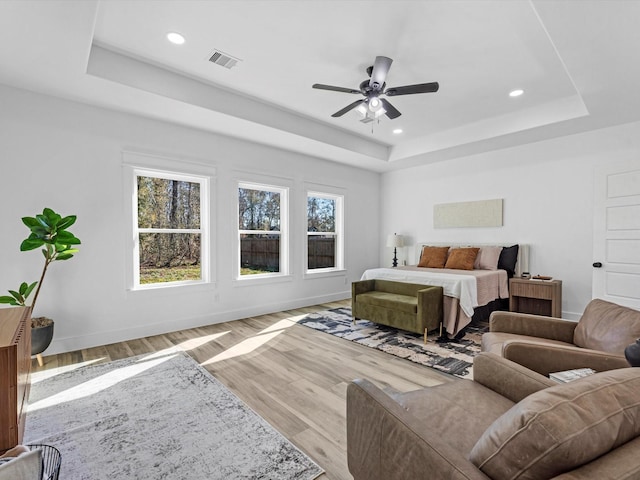 bedroom with ceiling fan, light hardwood / wood-style floors, and a tray ceiling