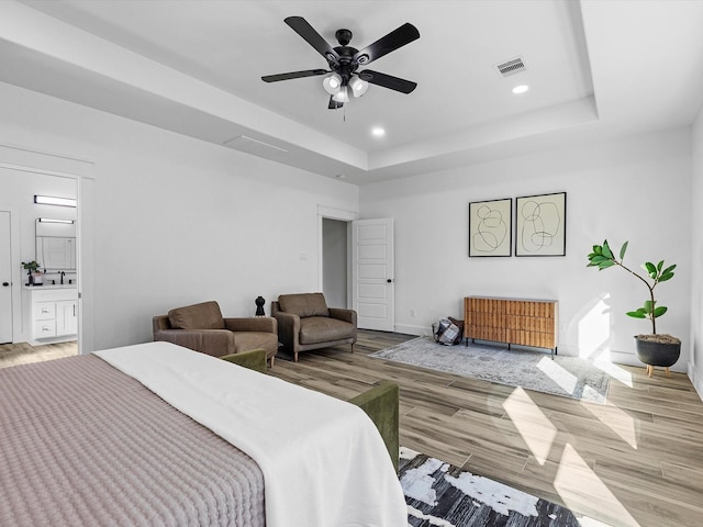 bedroom featuring connected bathroom, a tray ceiling, light hardwood / wood-style flooring, and ceiling fan