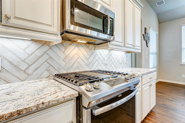 kitchen with tasteful backsplash, light stone countertops, appliances with stainless steel finishes, and light hardwood / wood-style flooring