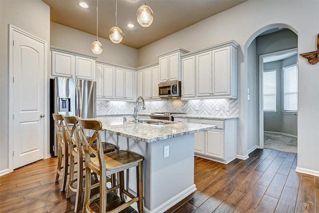 kitchen featuring decorative backsplash, an island with sink, decorative light fixtures, light stone counters, and stainless steel appliances