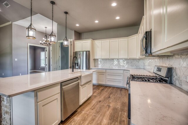 kitchen featuring light stone countertops, stainless steel appliances, white cabinetry, hanging light fixtures, and an island with sink