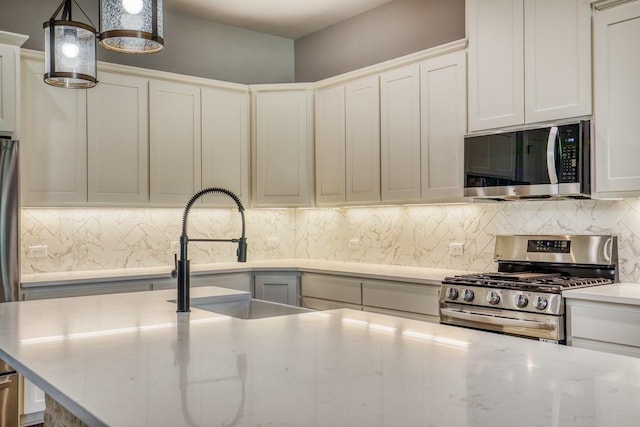 kitchen with appliances with stainless steel finishes, tasteful backsplash, sink, pendant lighting, and white cabinets