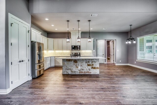 kitchen featuring tasteful backsplash, stainless steel appliances, dark wood-type flooring, decorative light fixtures, and an island with sink